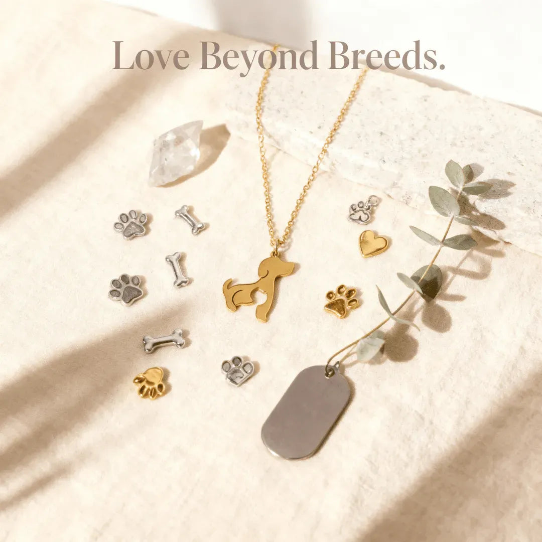 Gold and silver pet-themed jewelry on a beige fabric background with 'Love Beyond Breeds' text.