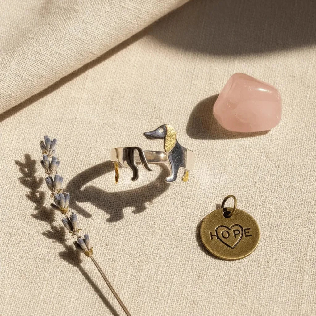 Dog-shaped brooch, 'HOPE' charm, and pink crystal on a beige fabric background