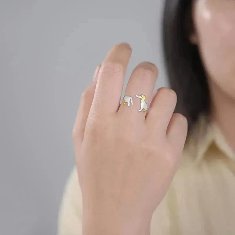 Hand wearing a ring with a small dog design on a plain background