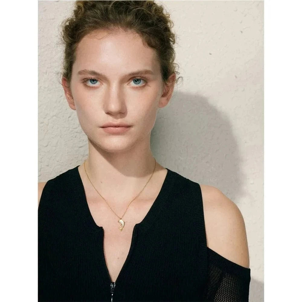 Woman wearing a black sleeveless top and gold necklace against a neutral background