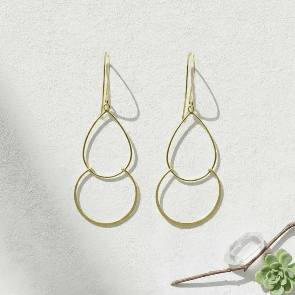 Gold hoop earrings on a light gray background with a small plant.
