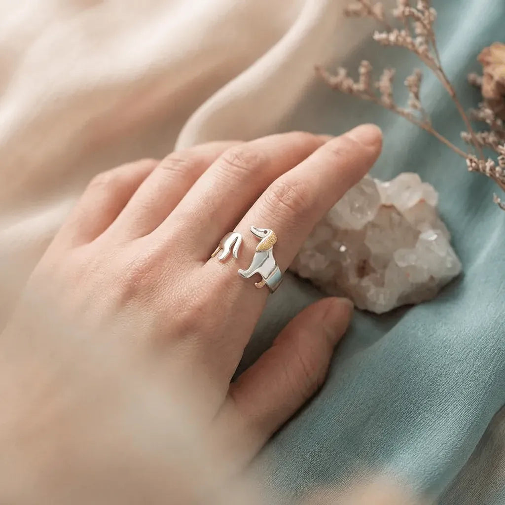 Hand wearing a silver ring with a small animal design on a soft fabric background