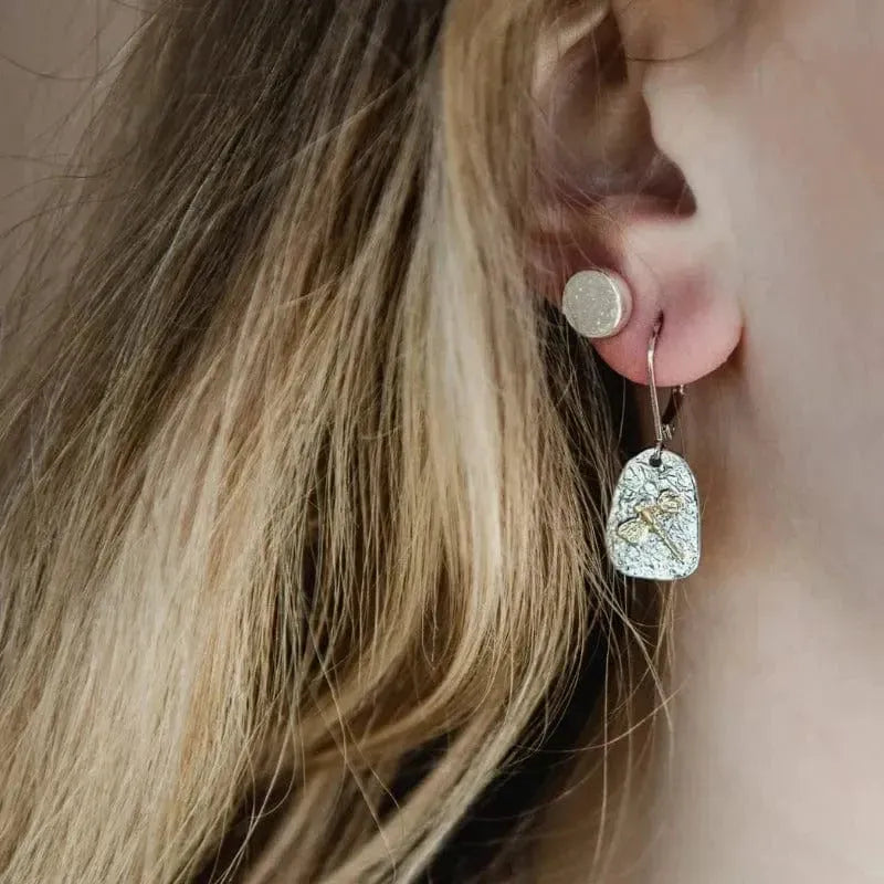 Close-up of a person wearing silver earrings with a cross design.