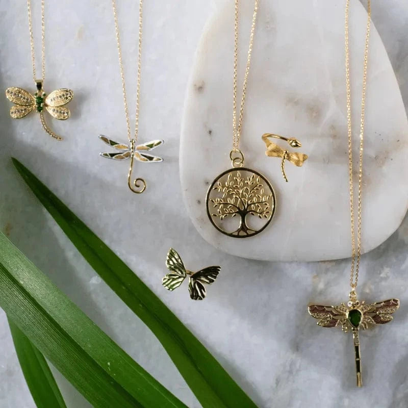 Gold necklaces with various pendants on a marble surface with green leaves.
