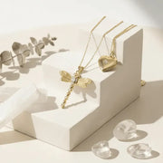 Gold necklace with a dragonfly pendant on a white surface with light shadows