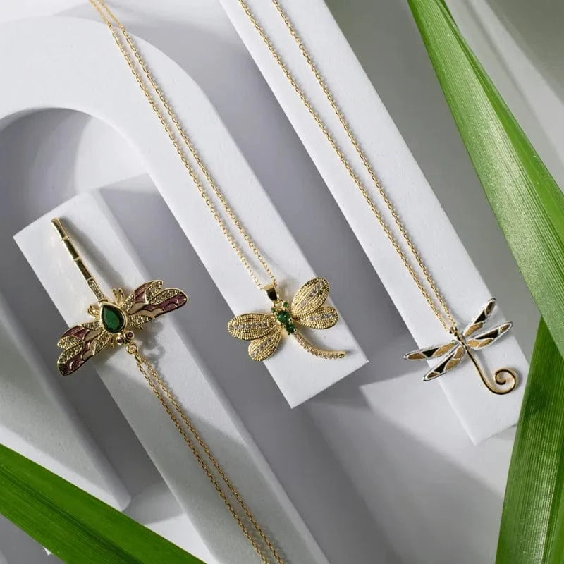 Three gold insect-shaped necklaces on a white surface with green leaves.