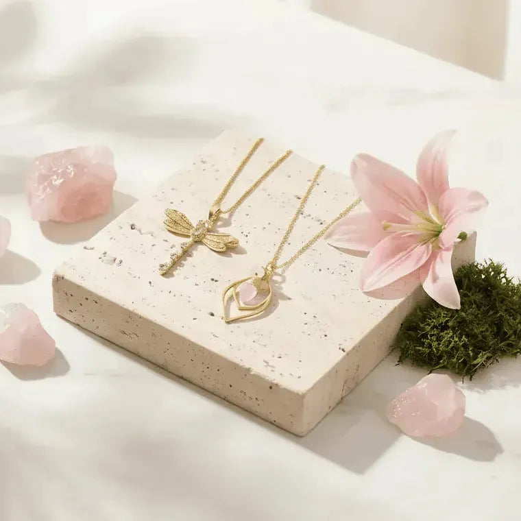 Gold necklaces on a stone surface with pink flowers and crystals