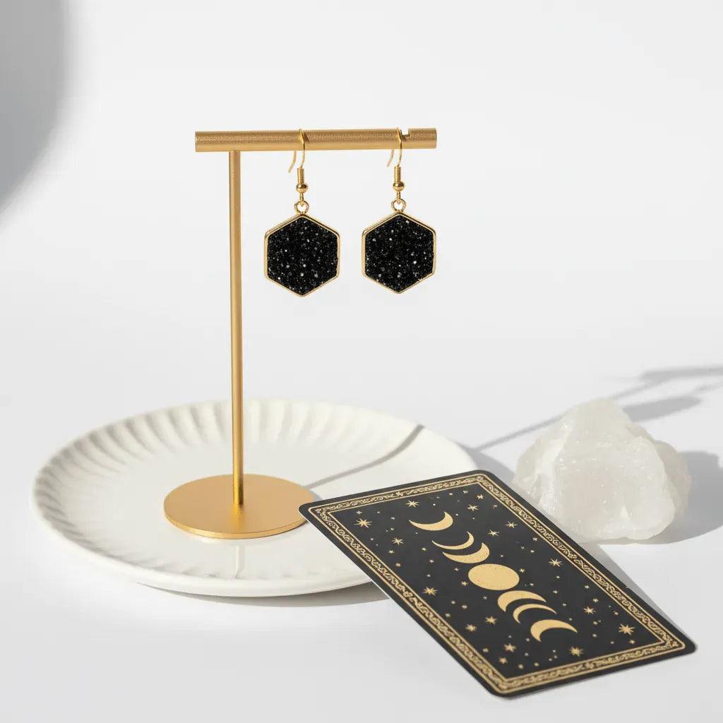 Black hexagonal earrings on a gold stand with a tarot card and crystal on a white background
