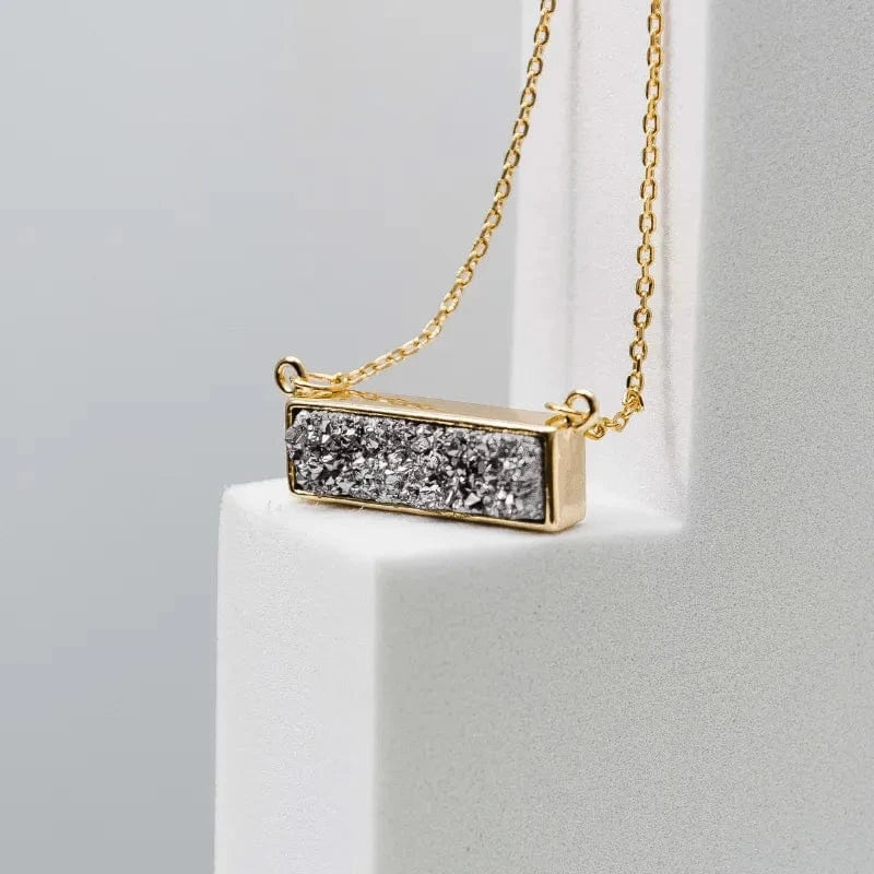 Gold necklace with a rectangular pendant on a gray background