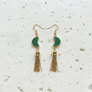 Gold and green tassel earrings on a white speckled surface