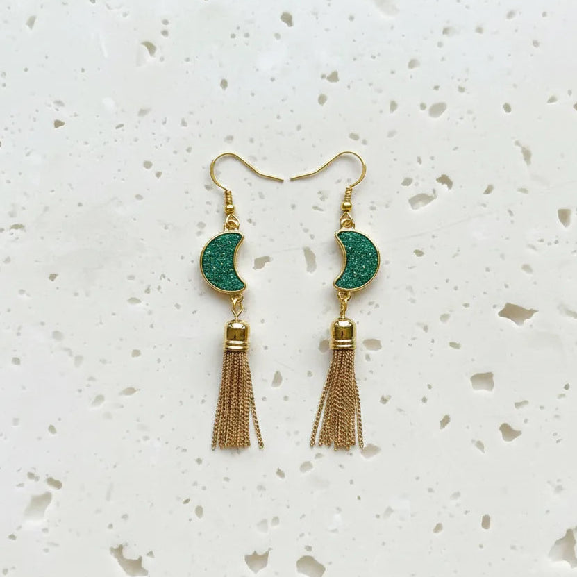 Gold and green tassel earrings on a white speckled surface