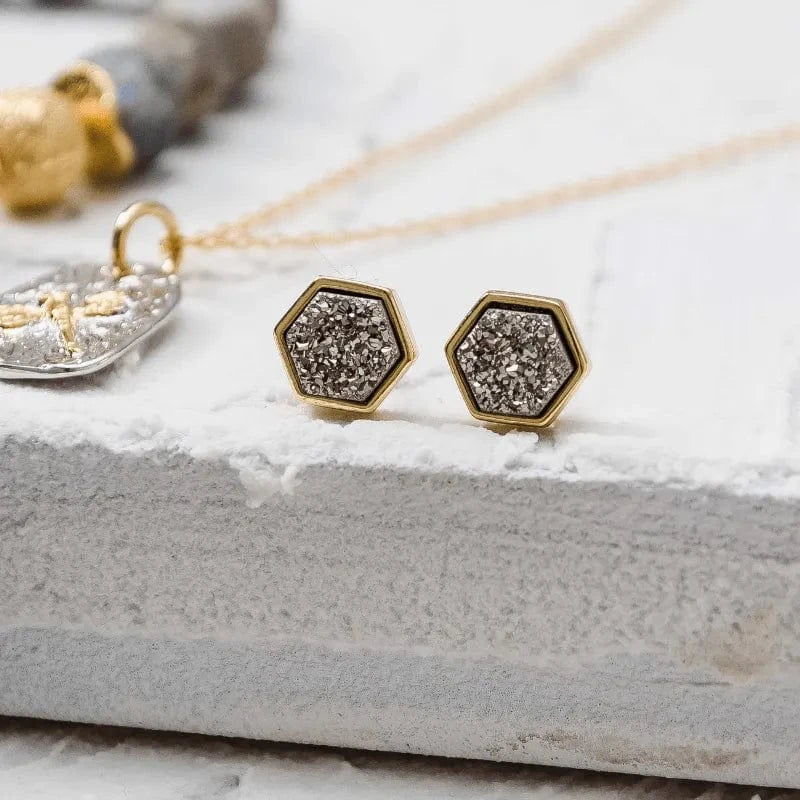 Hexagonal gold earrings with druzy stones on a textured surface