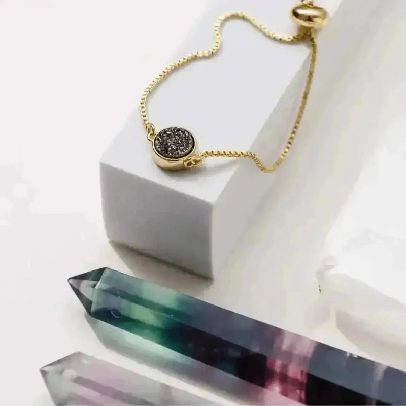 Gold bracelet with a gemstone on a white surface with crystal-like objects.