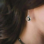 Close-up of a person wearing a silver earring with a green gemstone.