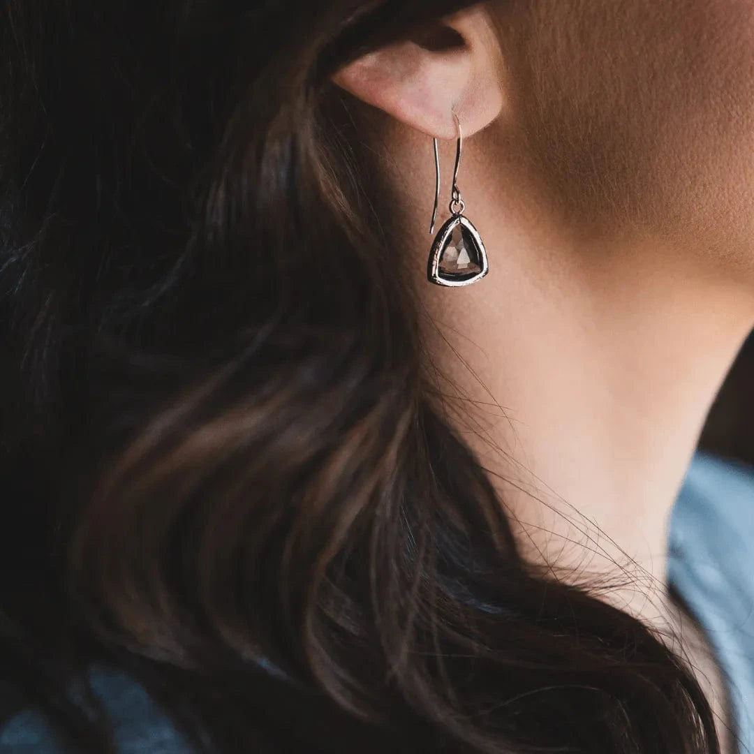 Close-up of a person wearing a teardrop-shaped earring with a dark stone.