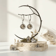 Silver earrings on a decorative stand with stones and leaves