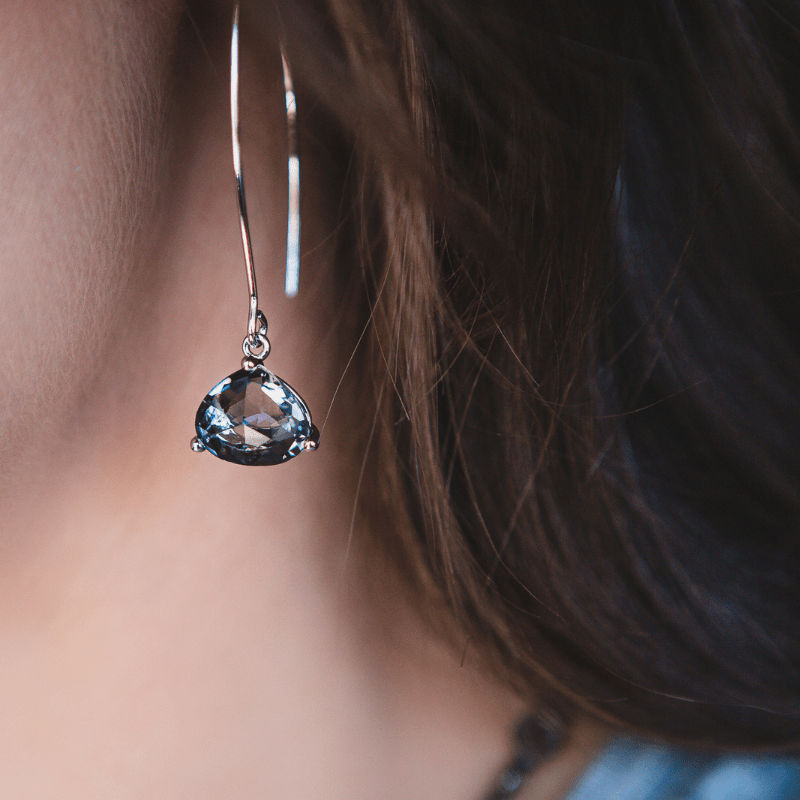 Teardrop-shaped gemstone earring worn by a person with blurred background