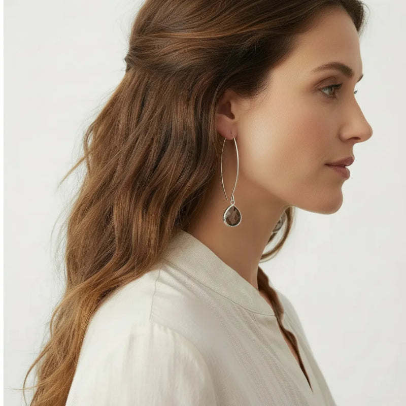 A woman in profile wearing a long, thin silver hoop earring with a teardrop- 