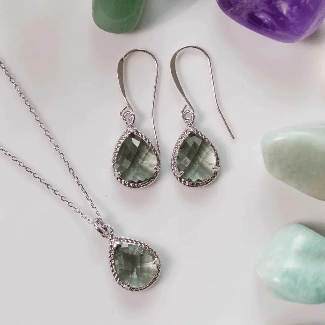 Teardrop-shaped green gemstone jewelry set with silver accents on a light background.