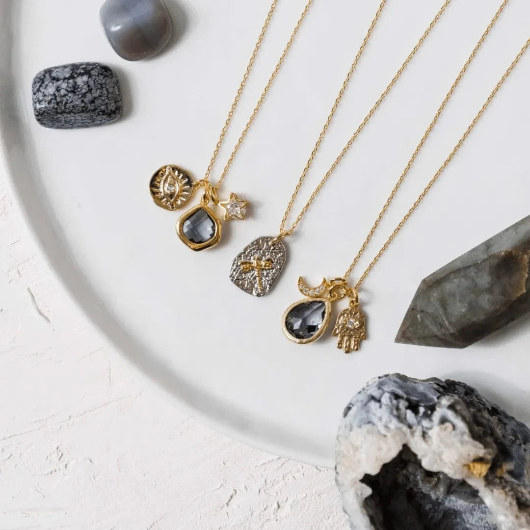 Gold necklaces with gemstone pendants on a white surface with crystals.
