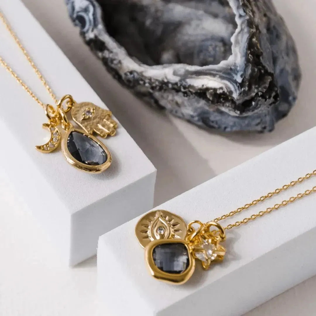 Gold necklaces with gemstone pendants on a white surface with decorative rock in the background