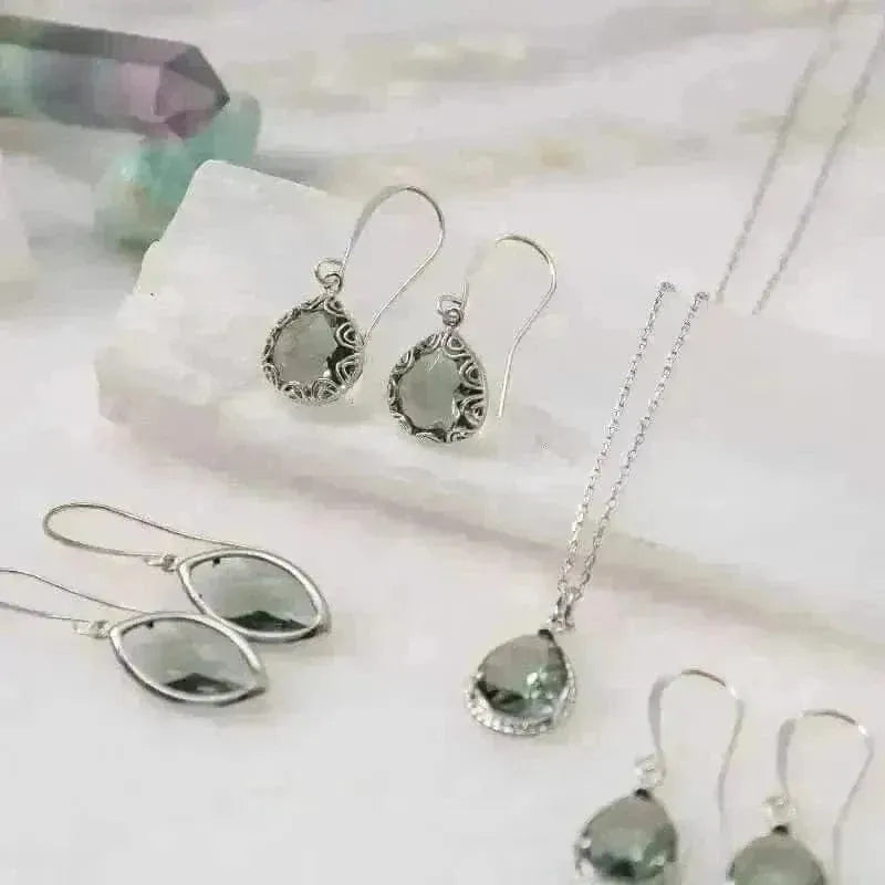 Elegant marquis silver dusk earrings with shimmering green stones displayed on a natural stone surface.