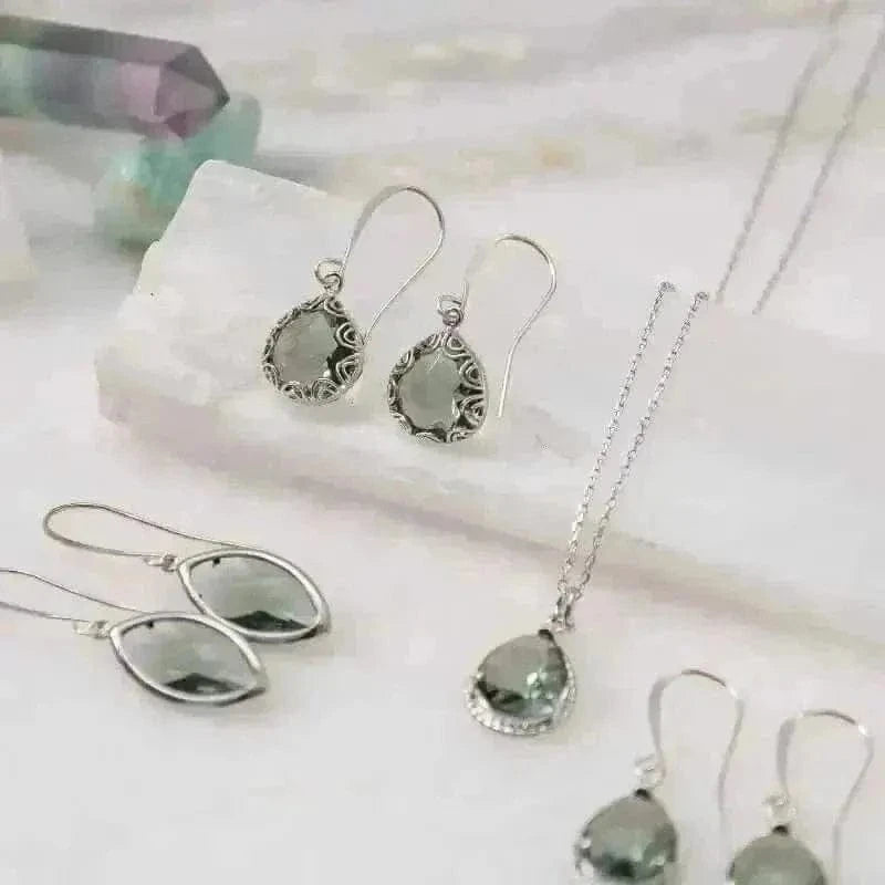 Elegant marquis silver dusk earrings with shimmering green stones displayed on a natural stone surface.