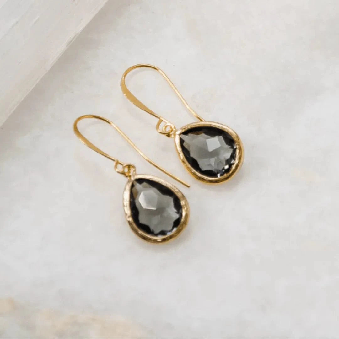 Gold earrings with black teardrop-shaped stones on a light background