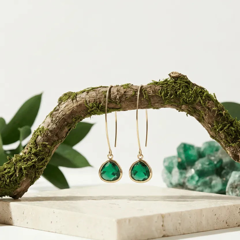 Green teardrop earrings hanging from a branch with green stones in the background
