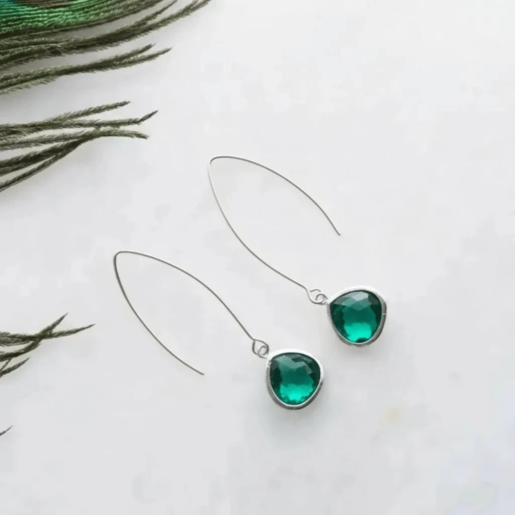 Green gemstone earrings on a white background with greenery