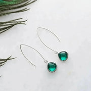 Green gemstone earrings on a white background with greenery