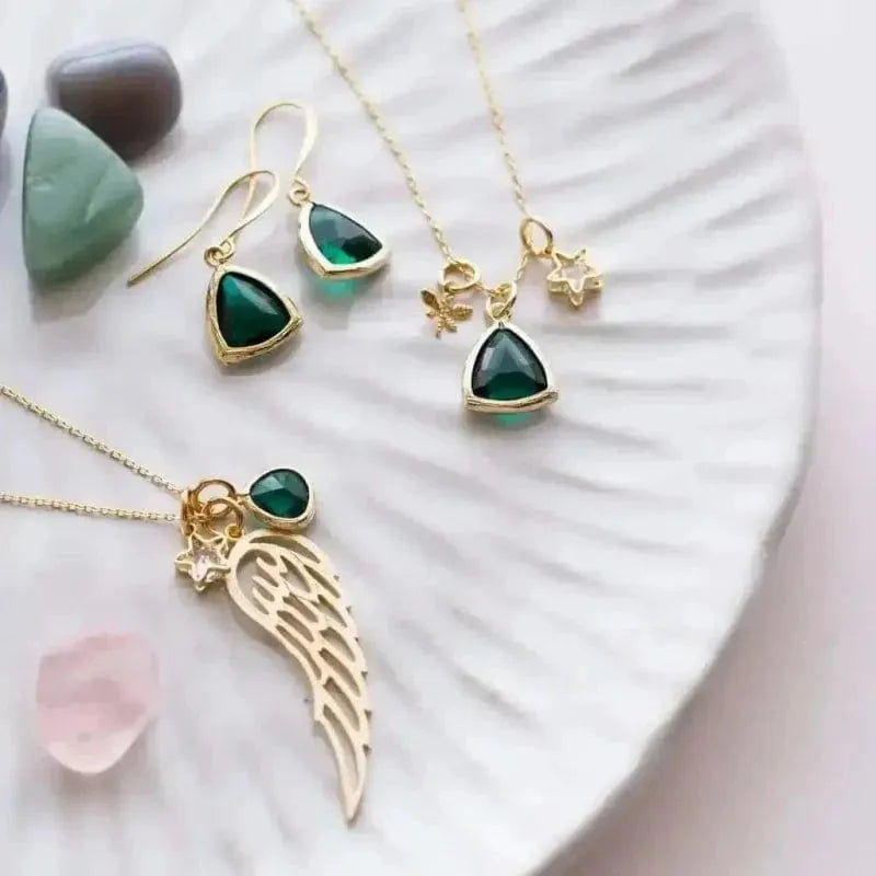 Gold jewelry set with green gemstones on a textured white surface