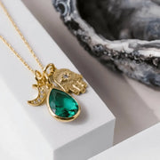 Gold necklace with a green teardrop pendant on a white surface