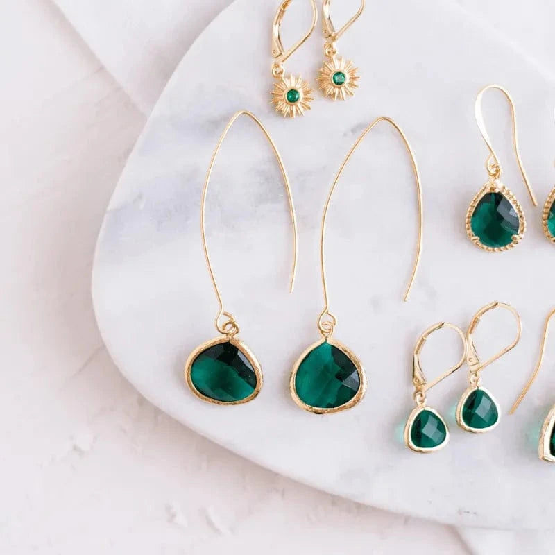 Gold earrings with green gemstones on a marble surface