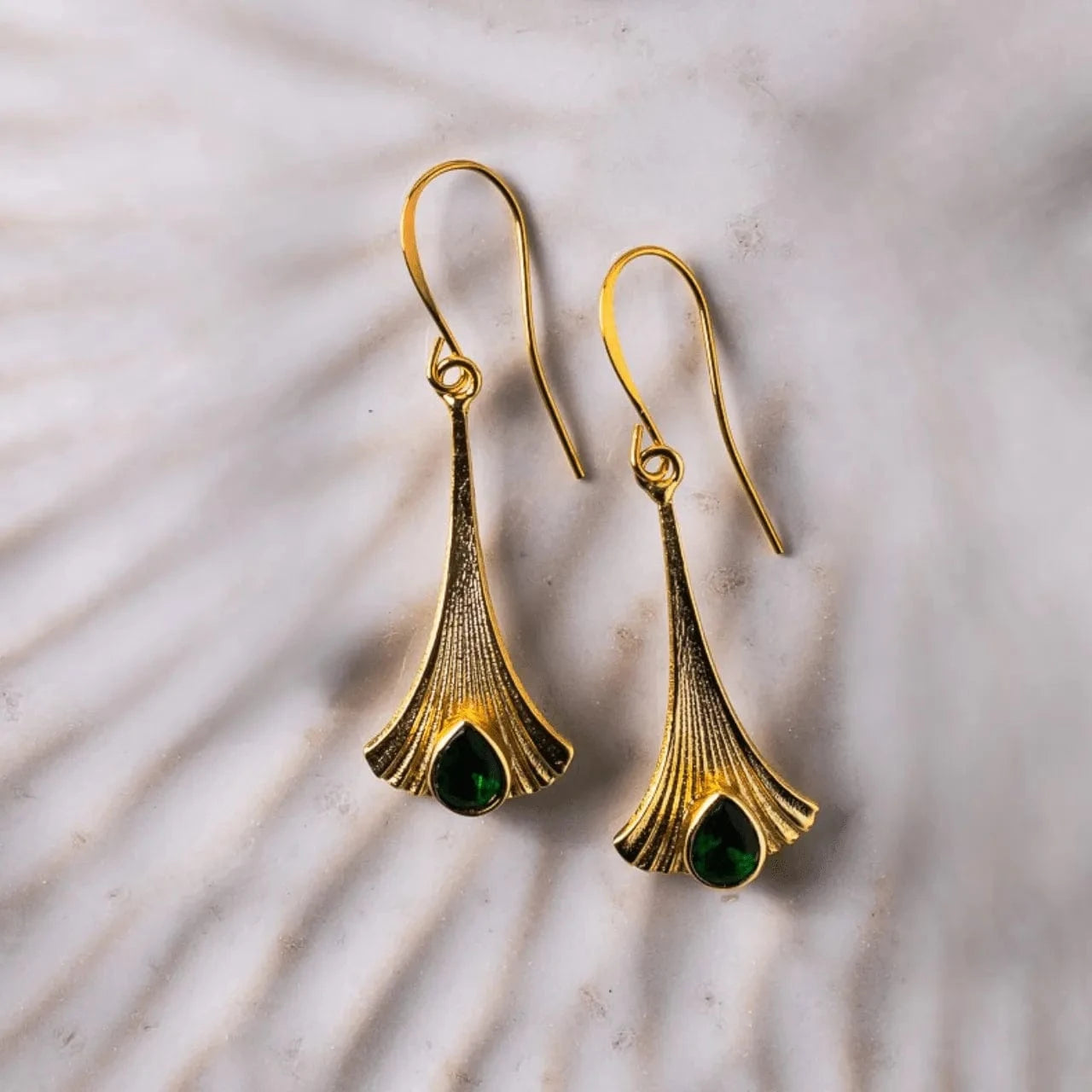 Gold earrings with green gemstones on a shell background
