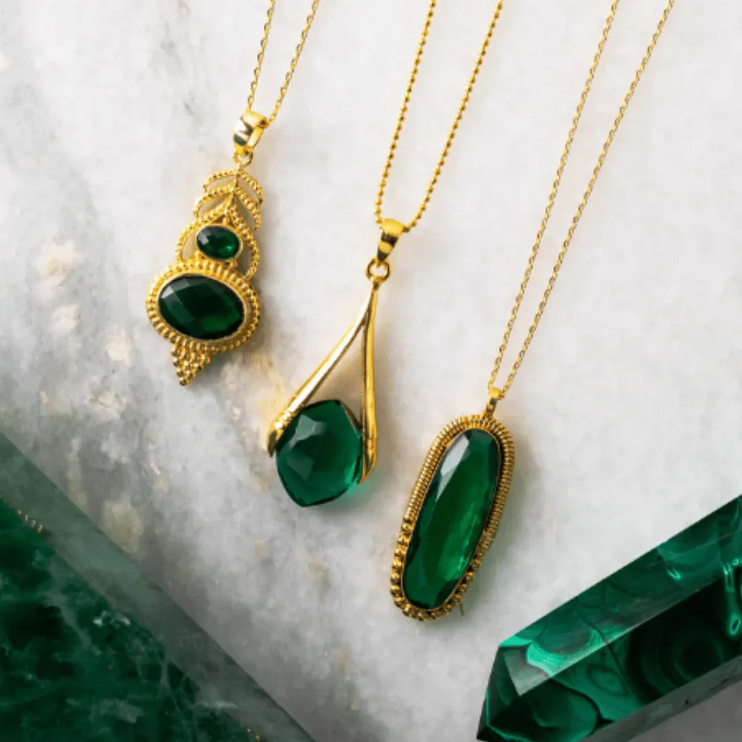 Gold necklaces with green gemstones on a marble surface