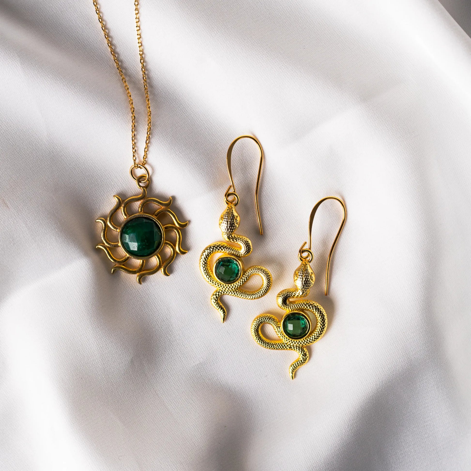 A pair of detailed gold-plated snake earrings adorned with faceted emerald green quartz gemstones, symbolizing transformation and renewal.