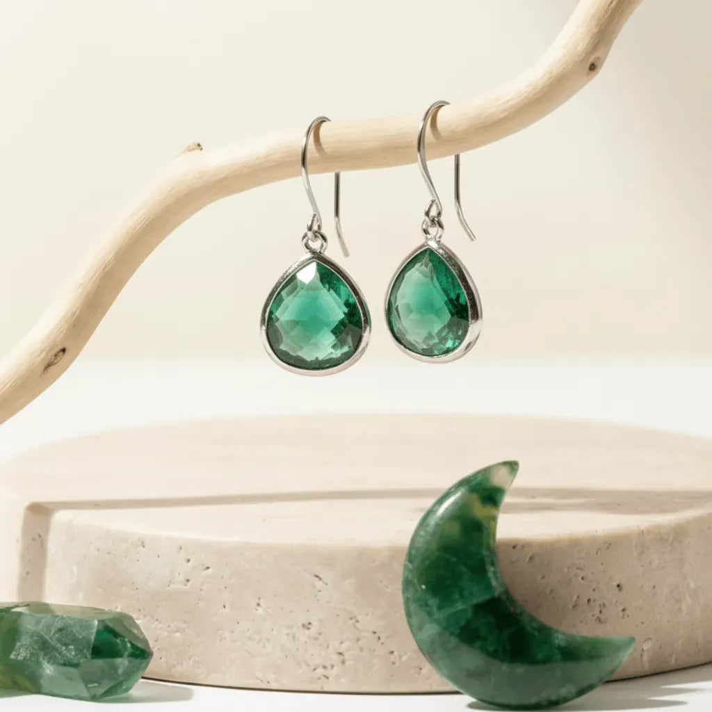 Green teardrop earrings on a wooden branch with a stone background