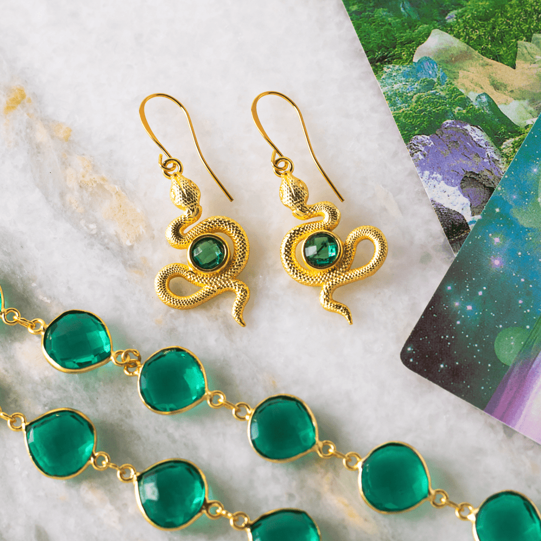 Gold and green jewelry set on a marble surface with nature-themed cards in the background