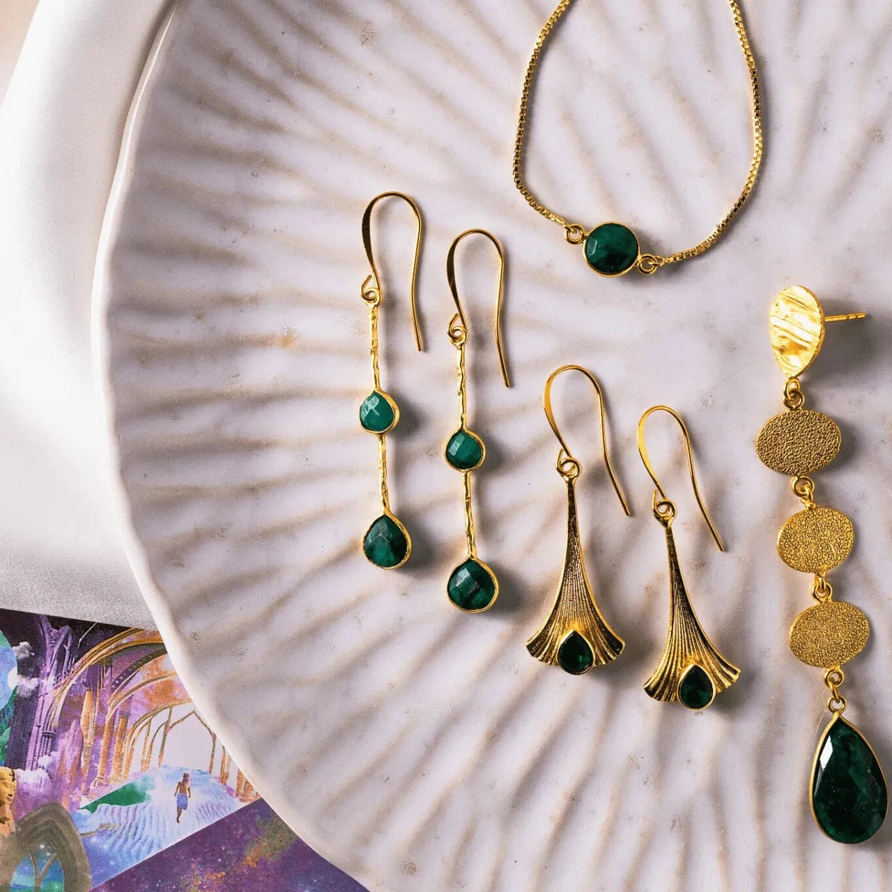 Gold and green jewelry set including earrings and a necklace on a textured surface.