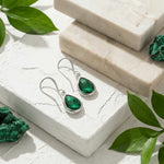 Green gemstone earrings and pieces on a white stone surface with green leaves.