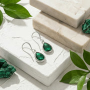 Green gemstone earrings and pieces on a white stone surface with green leaves.
