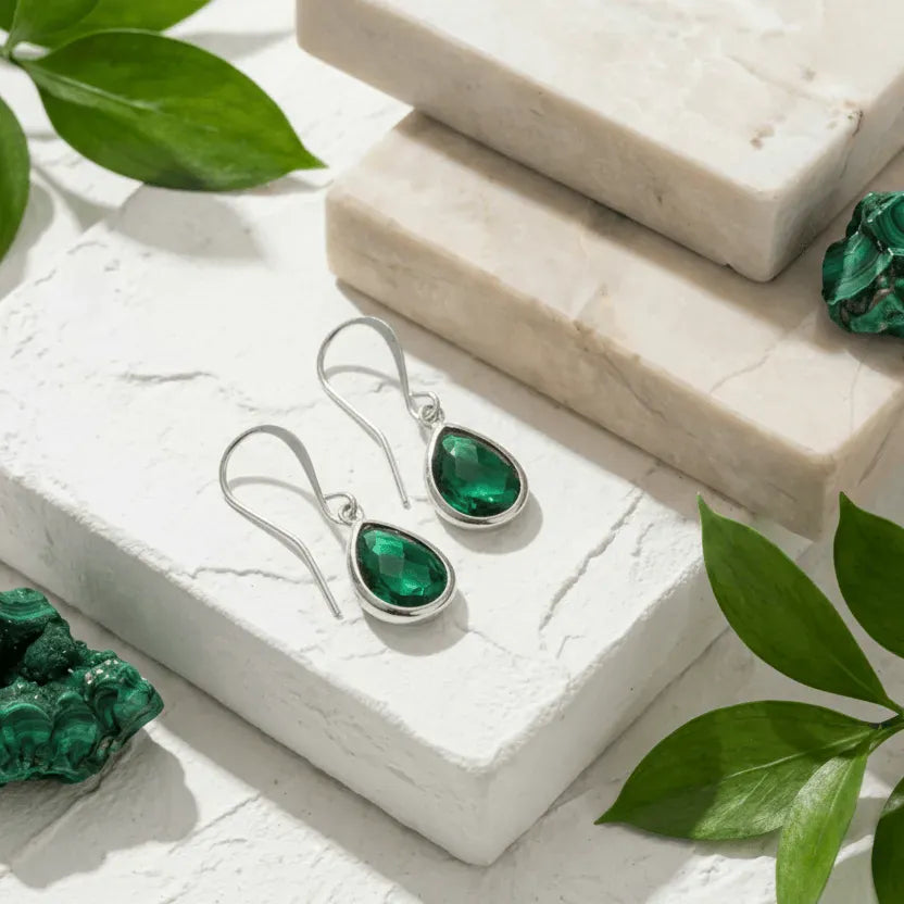 Green gemstone earrings and pieces on a white stone surface with green leaves.