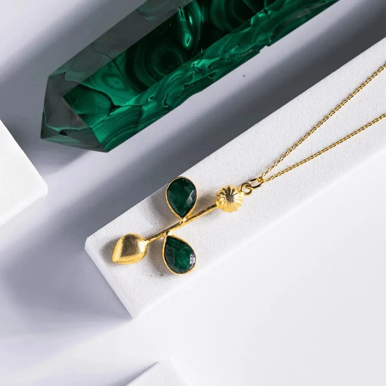 Gold necklace with green pendant on a white surface