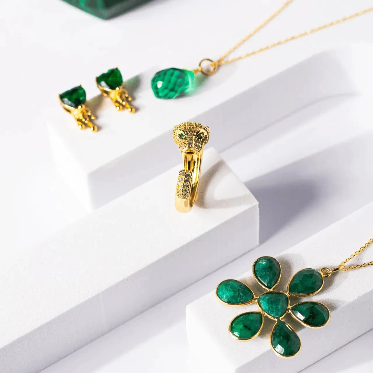 Gold jewelry set with emerald green stones on a white surface