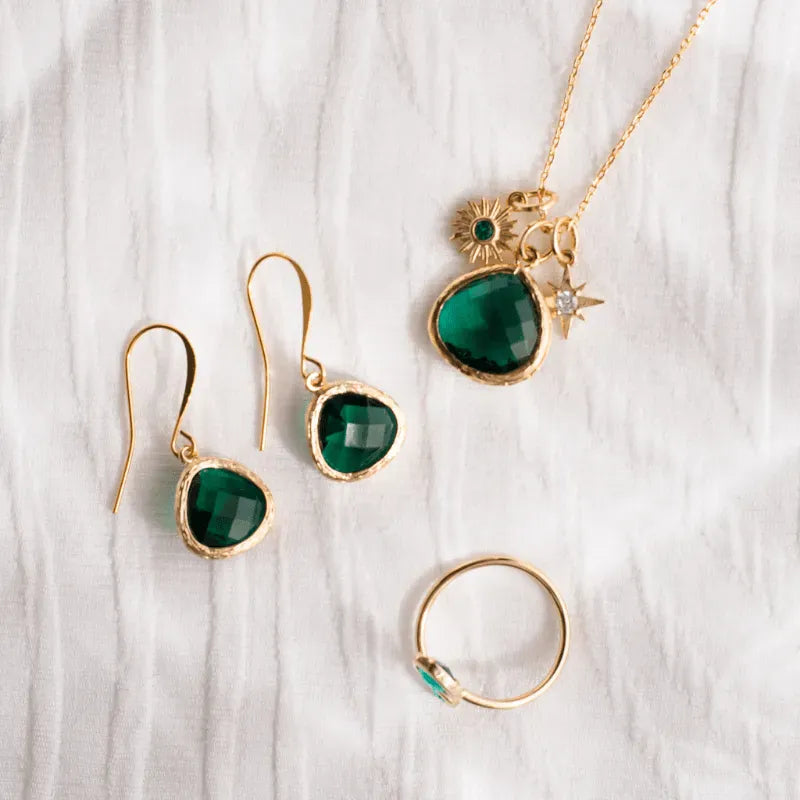 Gold jewelry set with green gemstones on a white fabric background