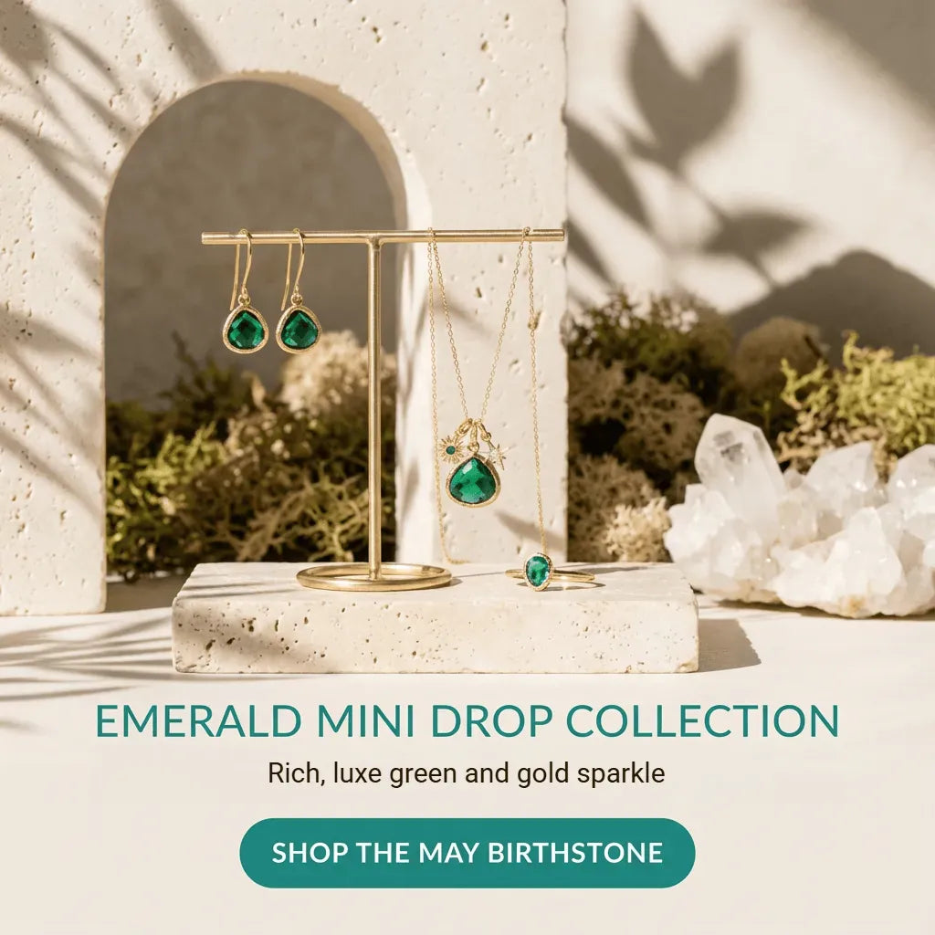 Jewelry display with emerald mini drop earrings and ring, set against a natural stone wall.