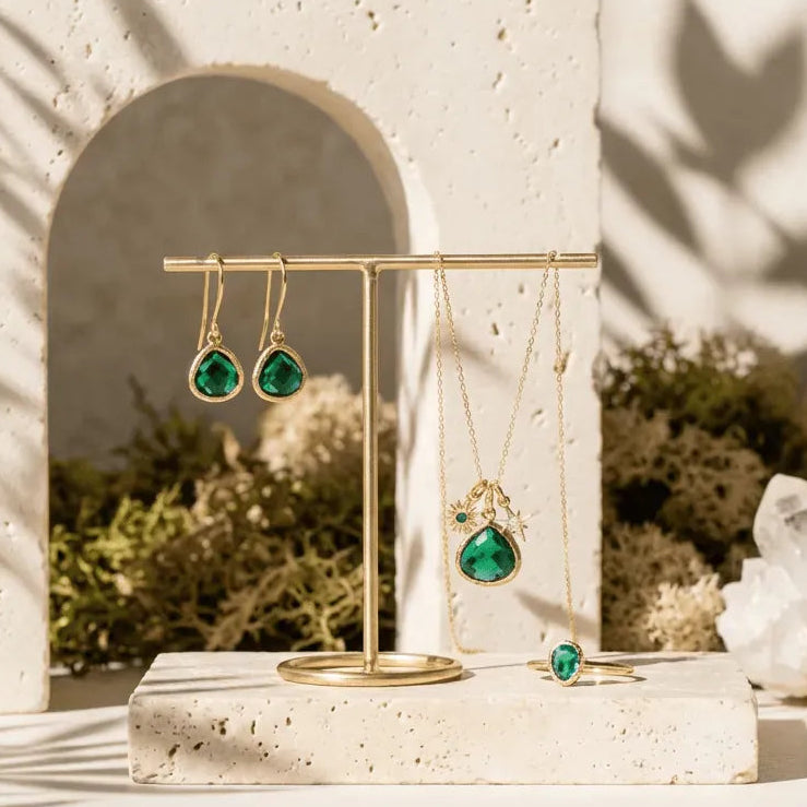 Jewelry display with emerald mini drop earrings and ring, set against a natural stone wall.