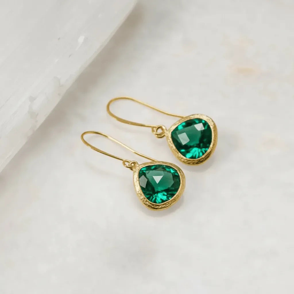 Gold earrings with green gemstones on a light background