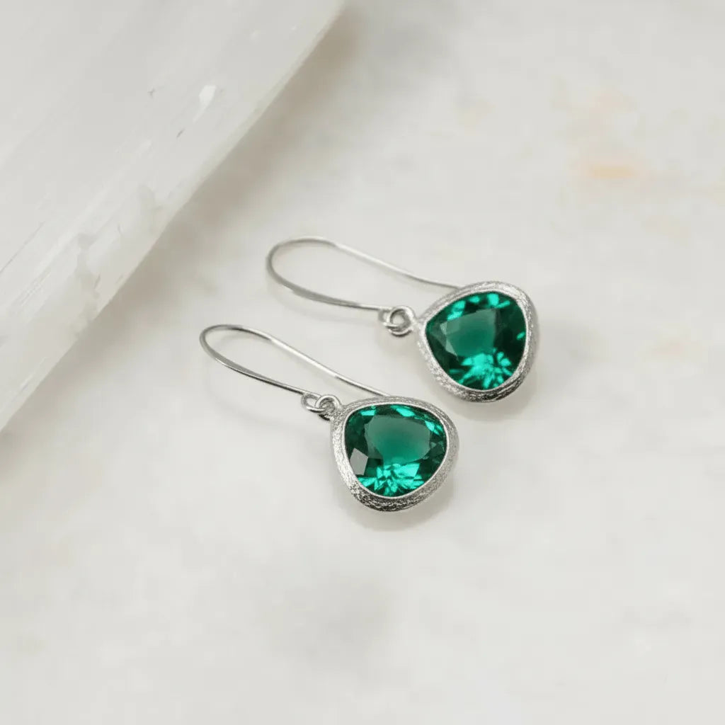 Silver earrings with green gemstones on a light background